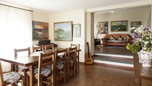 A dining area with wooden furniture and a guitar, a living room with a sofa and paintings, and a staircase leading to another level. -  "Pretty Farm" for 8 people in a farmhouse - ultra panoramic swimming pool      (Monsummano Terme)