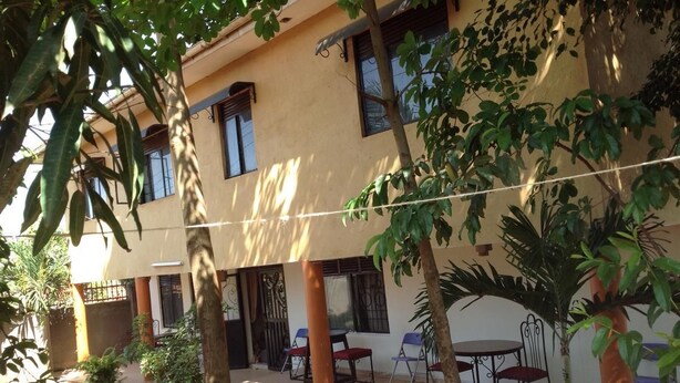 Un edificio con fachada color beige, numerosas ventanas y una terraza techada con sillas y mesas.