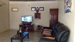 Una sala de estar con televisor, sofá, mesa de centro y una mesita con objetos decorativos.