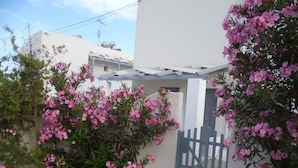 A residential area with a white building, a blue gate, and pink flowering shrubs. - Villa Katerina (Syros)