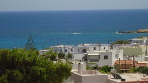 A coastal town with white buildings, a clear blue sea, and a distant rocky outcrop. - Villa Katerina (Syros)