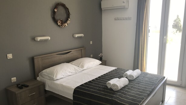 A neatly made bed with white linens, a dark striped blanket, and two rolled towels. - Villa Katerina (Syros)