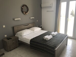 A neatly made bed with white linens, a dark striped blanket, and two rolled towels. - Villa Katerina (Syros)