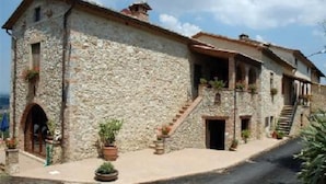A stone building with a staircase leading to a second floor, a small porch area, and potted plants.