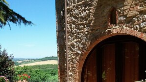 A stone building with a large arched door, a stone staircase, and a view of a hilly landscape.