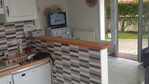 Une cuisine avec un mur recouvert de carreaux, un plan de travail en bois, un lave-vaisselle et un téléviseur posé sur un meuble.