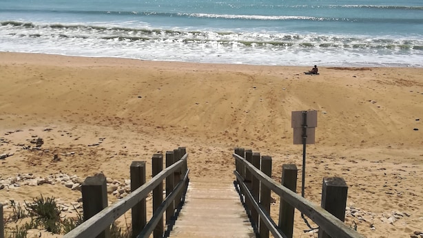 Une promenade en bois qui mène à une plage de sable, avec l’océan en arrière-plan.