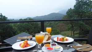 Una tavola apparecchiata per la colazione su un balcone con vista su un paesaggio montuoso.