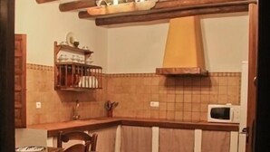 Eine Küche mit Fliesenboden, Holzstühlen, einer Mikrowelle und einem Regal mit Küchenutensilien.