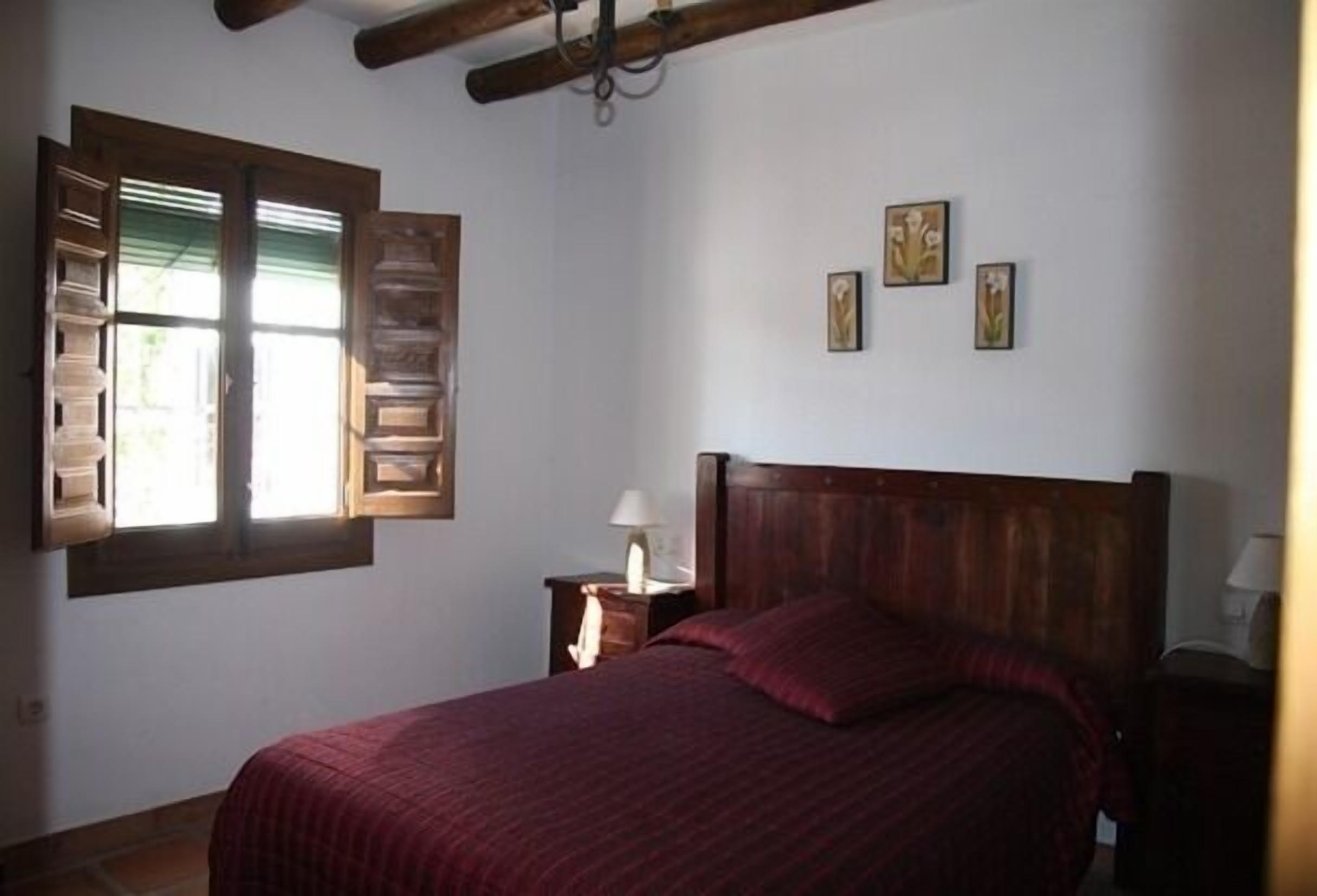 A bedroom with a wooden bed, a nightstand with a lamp, and a window with shutters.