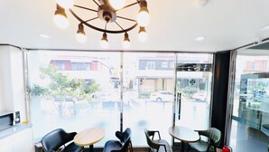Un interior moderno con área de cocina, asientos con mesas y grandes ventanales con vista a la calle.