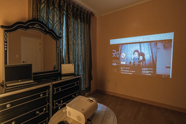 Una habitación con una computadora portátil sobre un tocador, un proyector proyectando una imagen en la pared y suelo de madera.