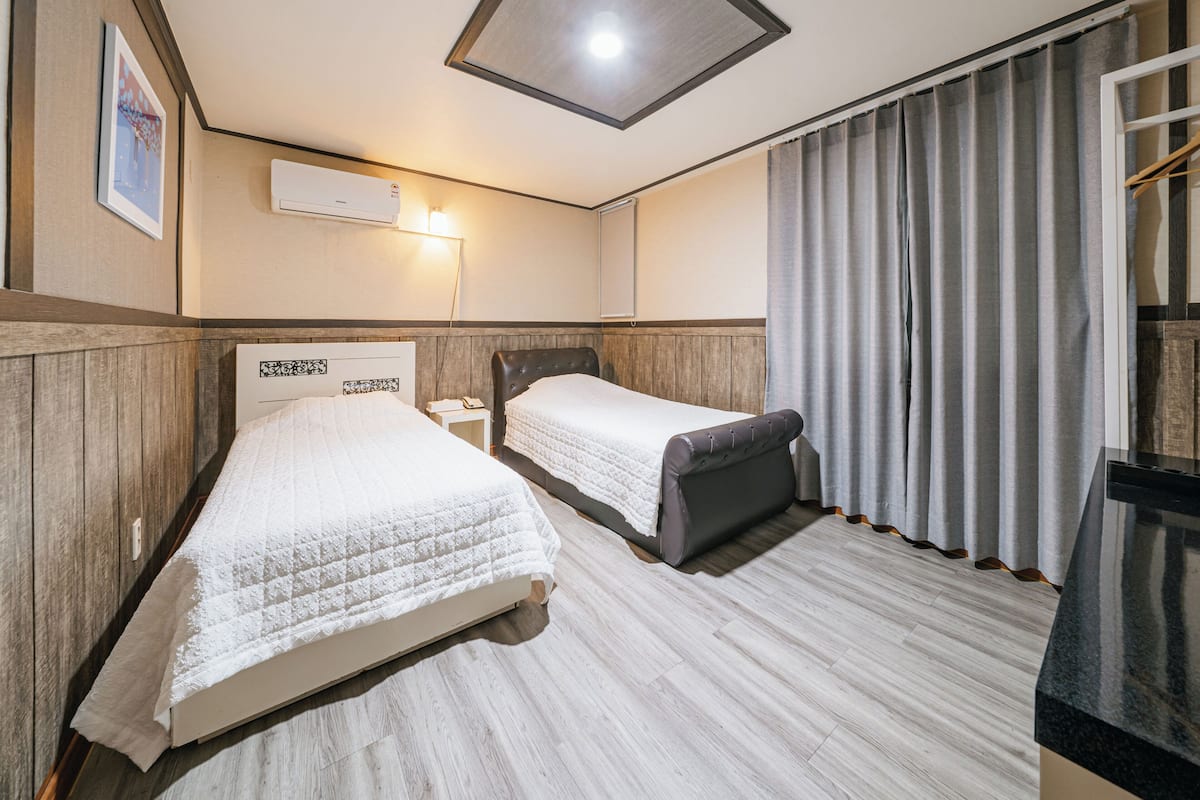 Habitación de hotel con dos camas, piso de madera, aire acondicionado de pared y una cortina en la ventana.
