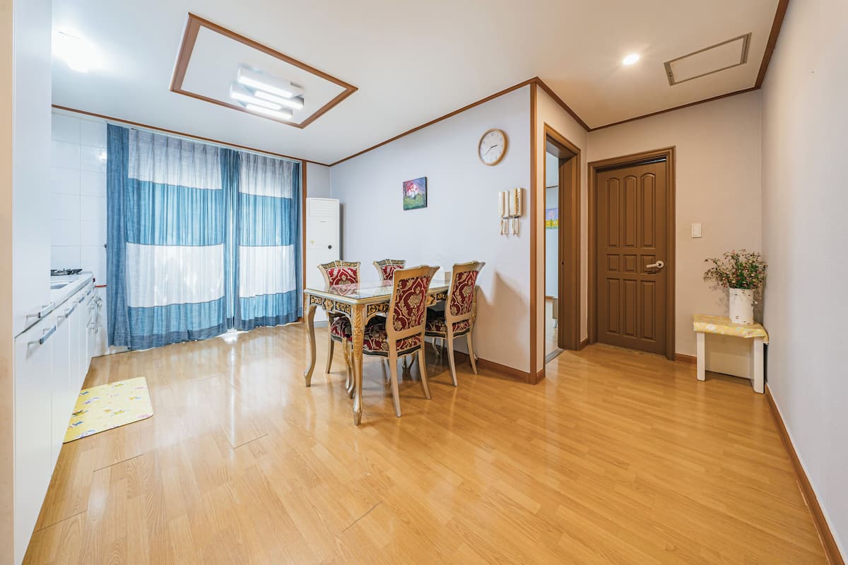 Un comedor con una mesa y sillas de madera, un reloj en la pared y una puerta que da a otra habitación.