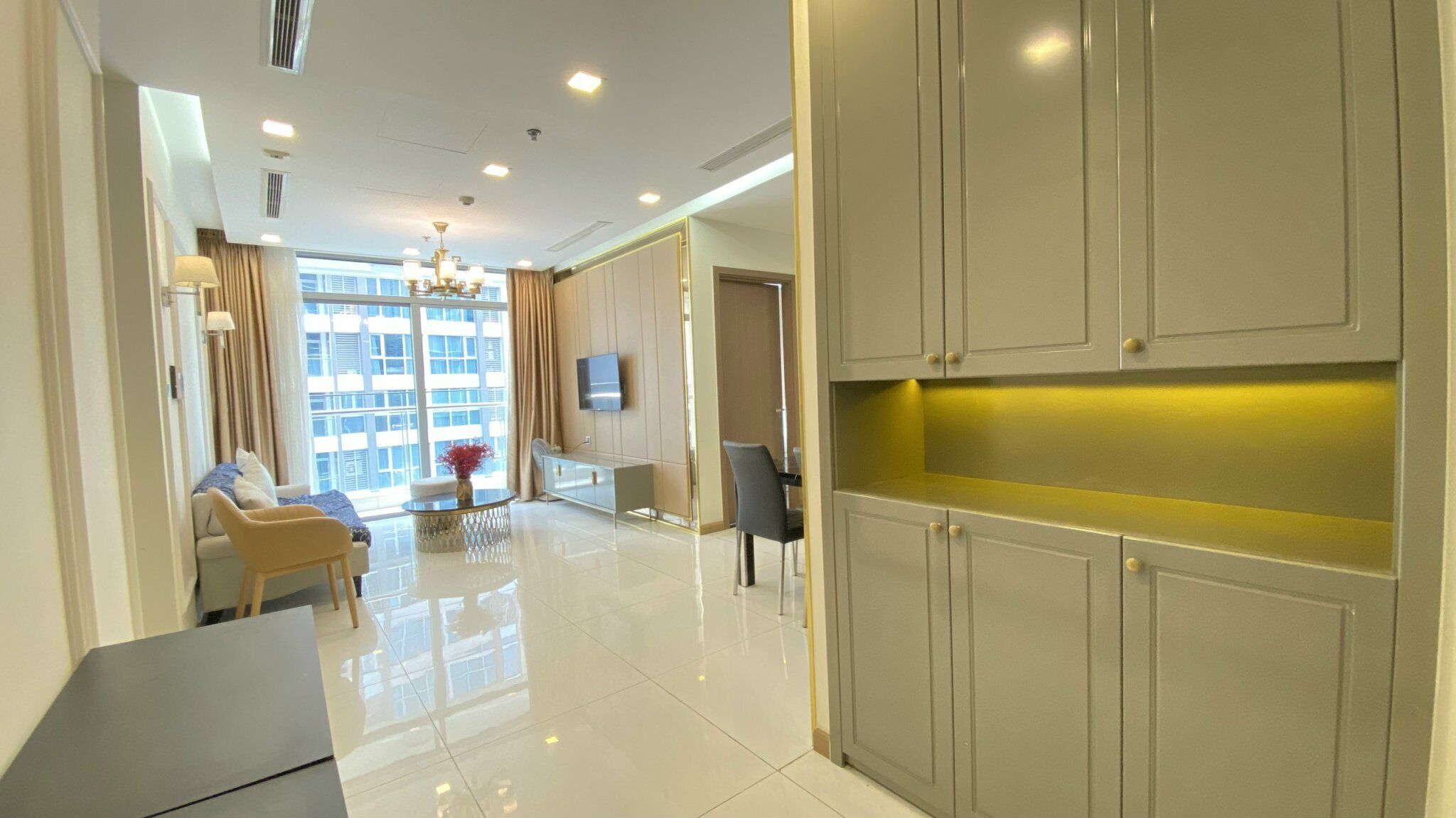 A modern hotel room with a large window, a dining area, and a kitchen.
