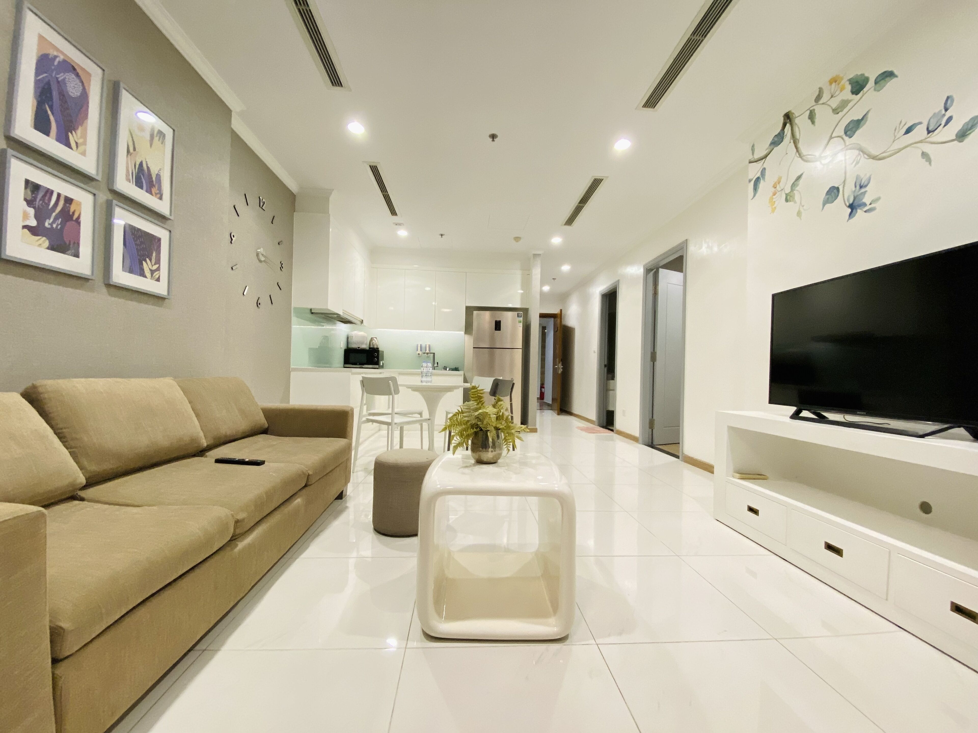 A modern living room with a beige sofa, a white coffee table, and a flat-screen TV on a white stand.