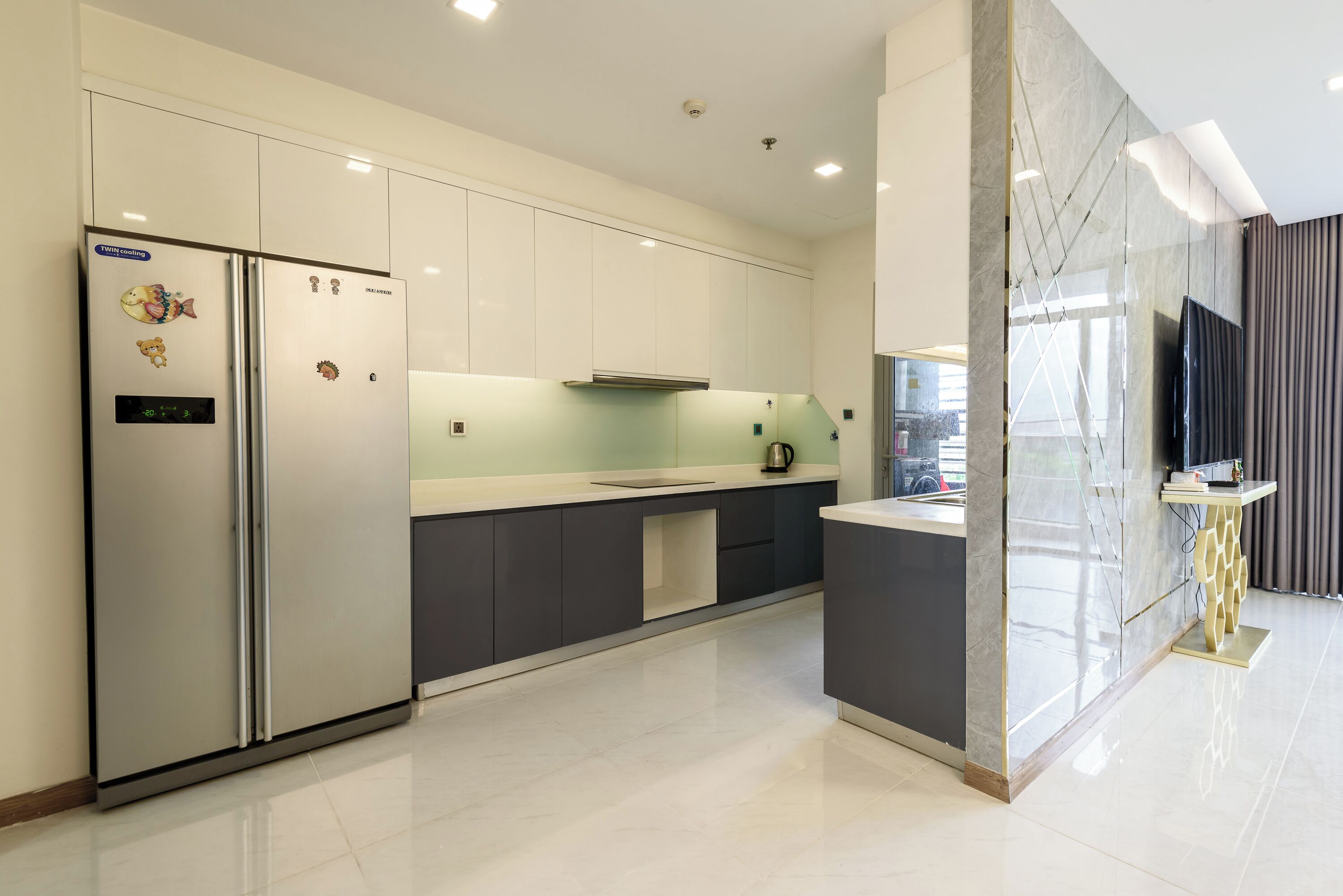 Eine moderne Küche mit einem Edelstahl-Kühlschrank, einer Mikrowelle und einem eingebauten Backofen. Es gibt eine graue Arbeitsplatte und eine Marmor-Spritzschutzwand.