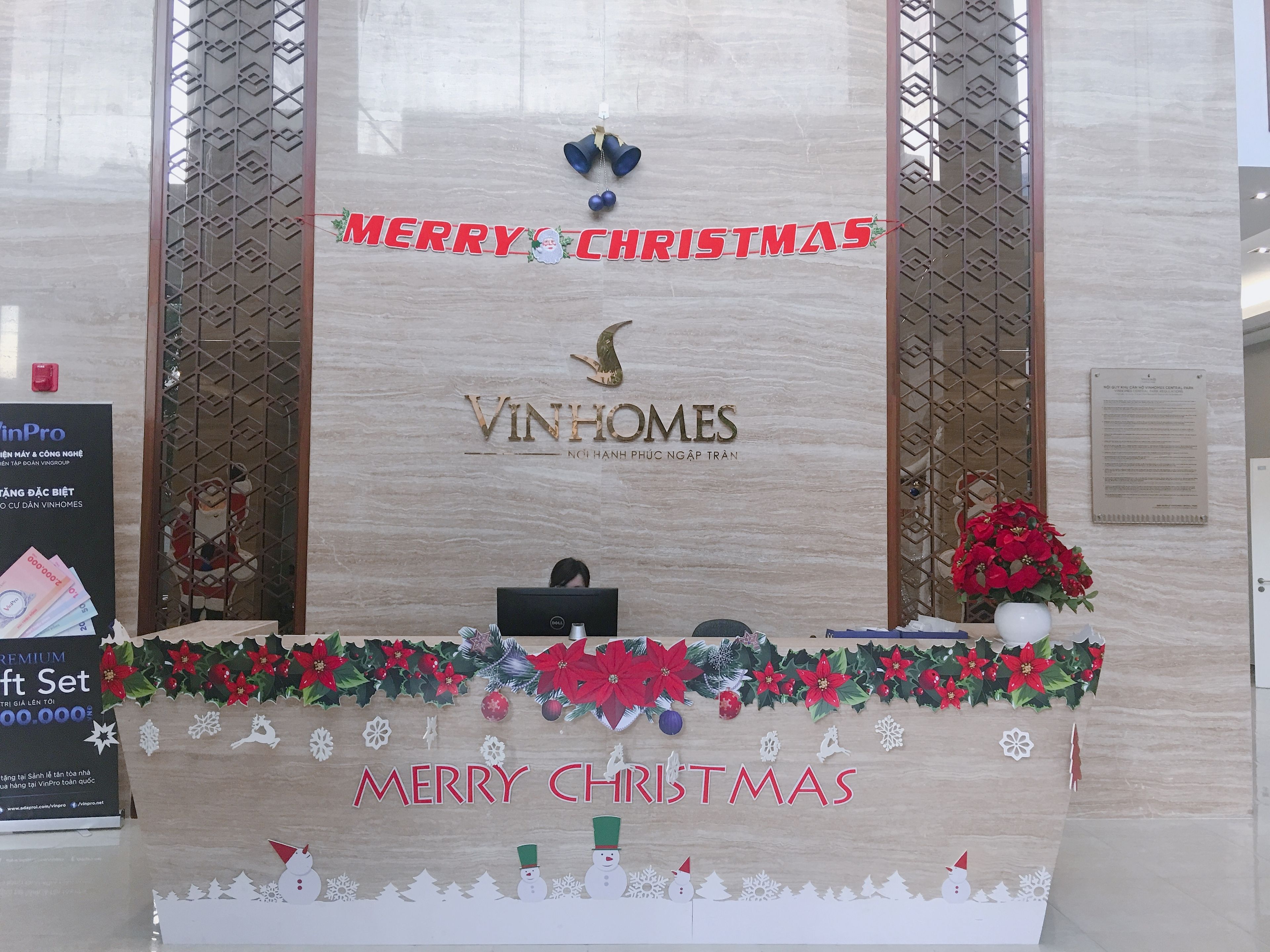 A reception desk with a 'Merry Christmas' sign, a logo for VinHomes, and a 'Premium Gift Set' sign.