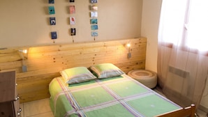 Un lit en bois surmonté d’une couvre-lit à rayures vertes et violettes, un petit tapis rond et une étagère murale où sont disposés divers objets.