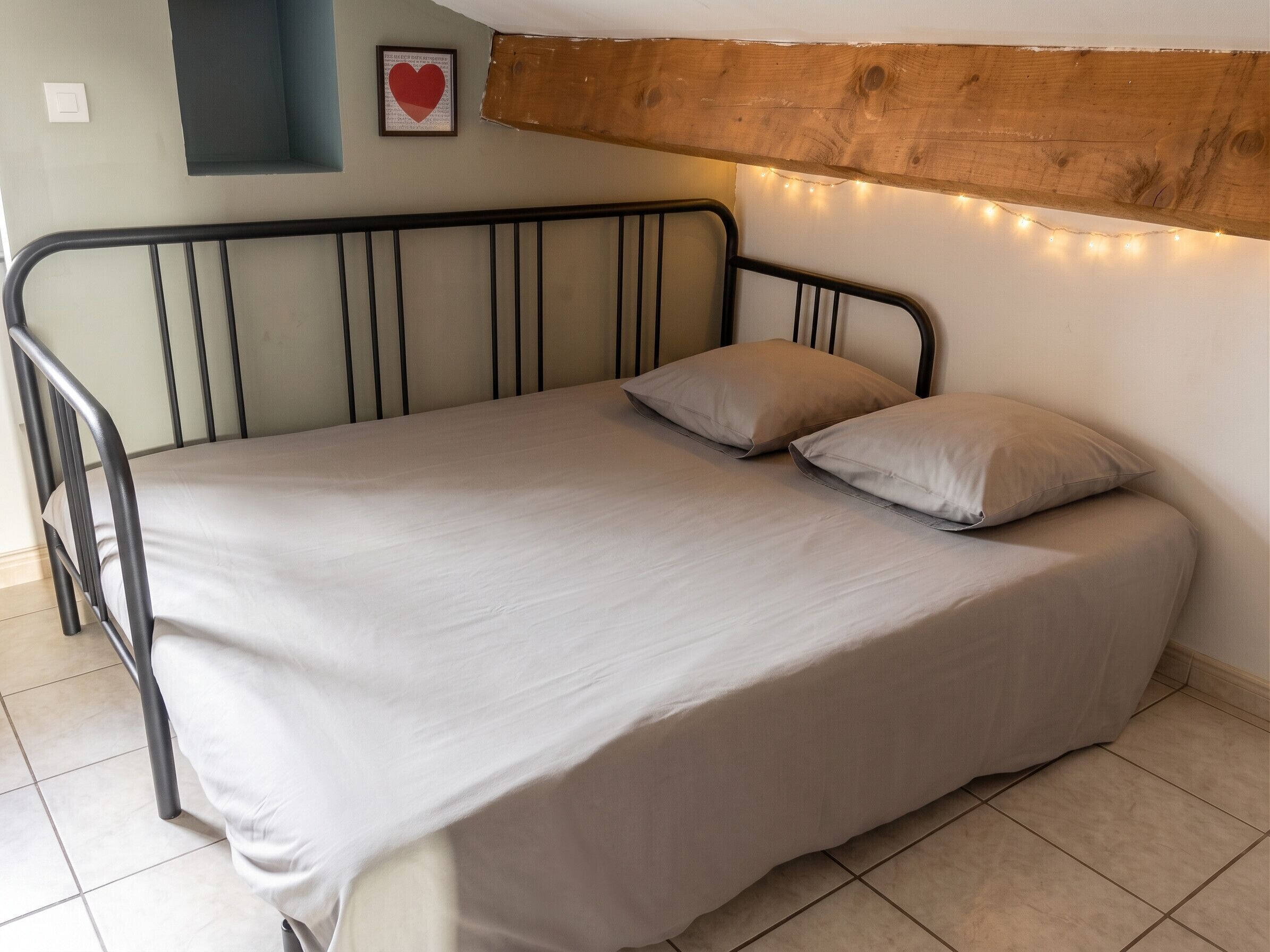 Un lit simple avec un cadre en métal, un matelas beige et deux oreillers.