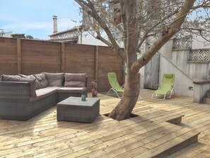 A wooden deck with a wicker sofa, two green lawn chairs, and a small table. - Homerez - House in Agde with Garden. (Agde)