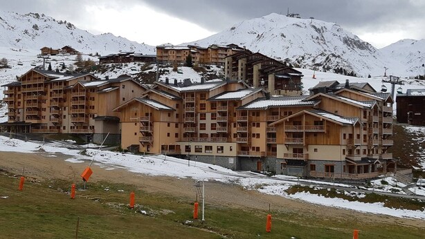 Un hotel de varios pisos con estilo arquitectónico alpino tradicional, con balcones y un telesilla de esquí al fondo.