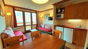 Una habitación compacta con una mesa de comedor de madera, un sofá, una pequeña cocina con microondas y una ventana con vistas a edificios.