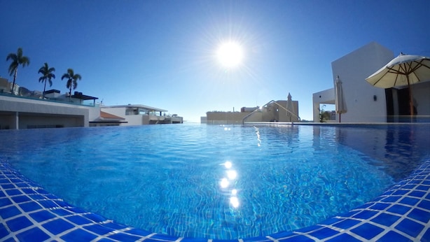 A swimming pool with clear blue water, surrounded by modern buildings and palm trees. - Modern Hideaway with Private Terrace in Old Town (Puerto Vallarta)