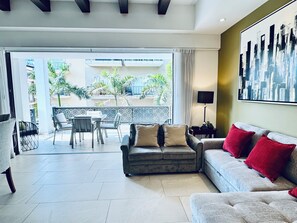 A modern living room with a sofa, a dining area, and a balcony with plants.
