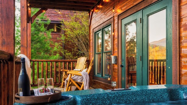 A wooden cabin with a hot tub, a chair, and a bottle of wine on a tray.