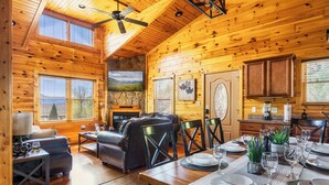 A wooden cabin interior with a dining area, kitchen, and living room.