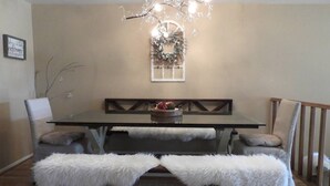 Un coin repas avec une table en bois, deux bancs rembourrés, un lustre et une guirlande décorative accrochée au mur.