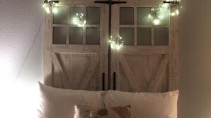 Un lit avec du linge de lit blanc et un coussin décoratif portant l’inscription « Marché aux Puces, Paris ».
