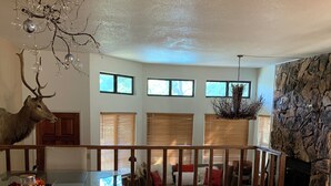 Un vaste salon comprenant une grande table à manger en bois, une cheminée en pierre et une tête de cerf accrochée au mur.