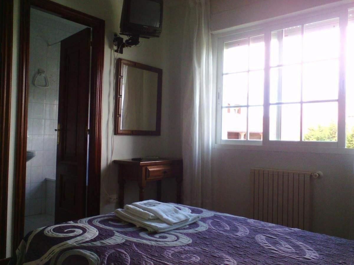 A bedroom with a bed, a bedside table, a mirror, a window with curtains, and a radiator.