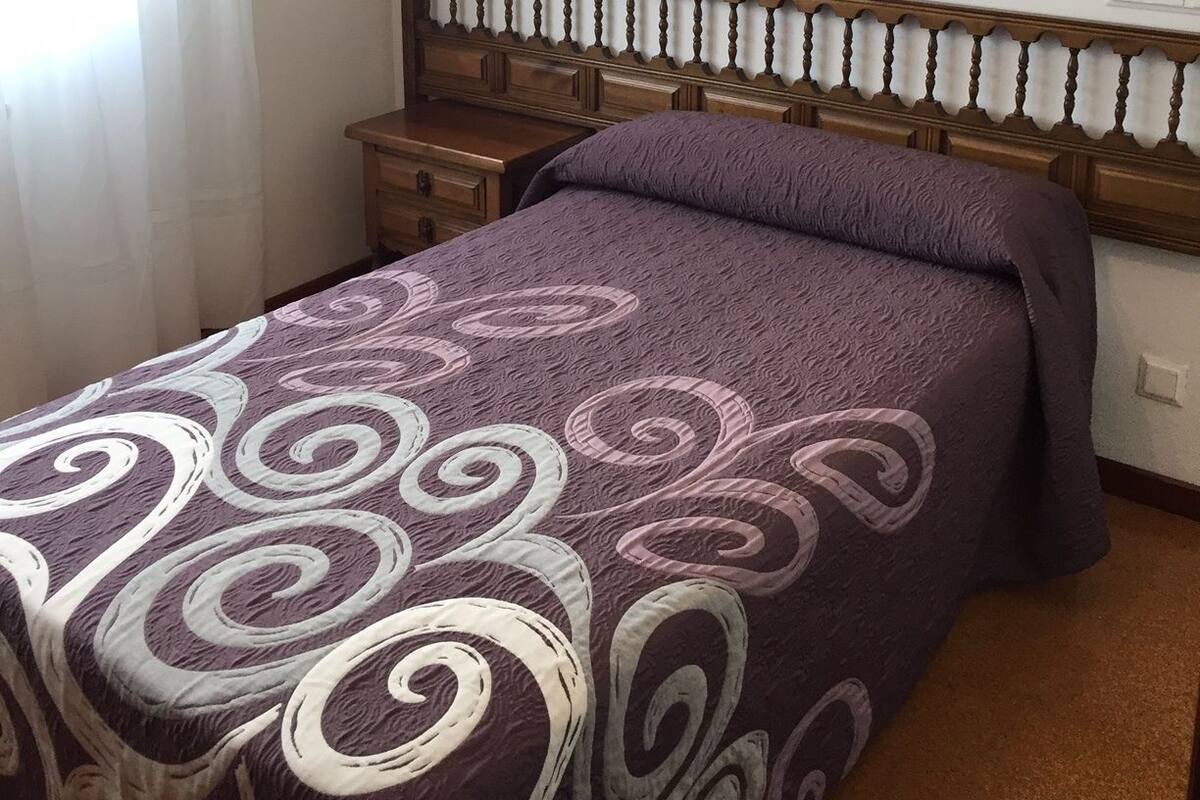 Un dormitorio con cama, mesitas de noche e iluminación en la pared.