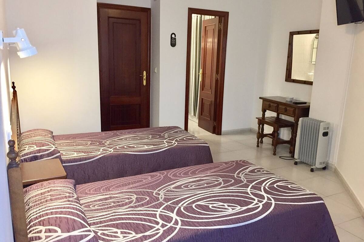Un dormitorio con dos camas, un escritorio, una silla, un radiador y un televisor montado en la pared.