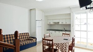 A compact kitchen with white cabinets, a dining table with a checkered tablecloth, and a blue sofa. - Pensión Rey (Isla de Arosa)