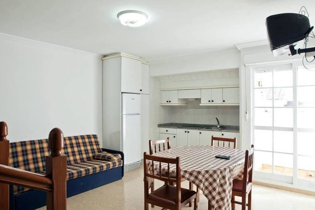 Una cocina compacta con armarios blancos, una mesa de comedor con mantel a cuadros y un sofá azul.