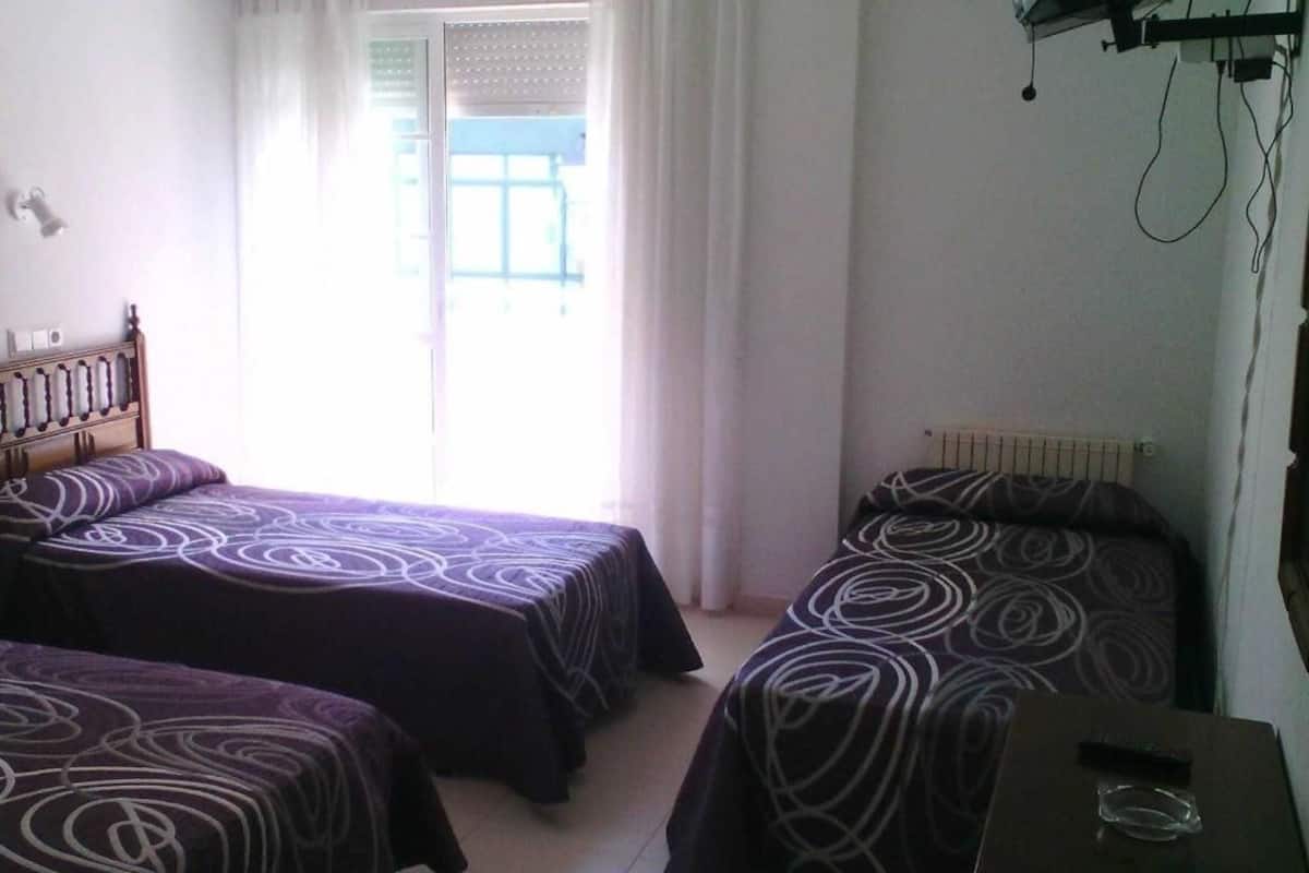 Una habitación con dos camas, cabecera de madera, ventana con cortinas y un radiador.