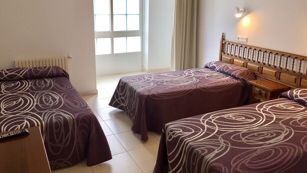 A hotel room with two beds, a wooden headboard, a nightstand, and a window with curtains. - Pensión Rey (Isla de Arosa)