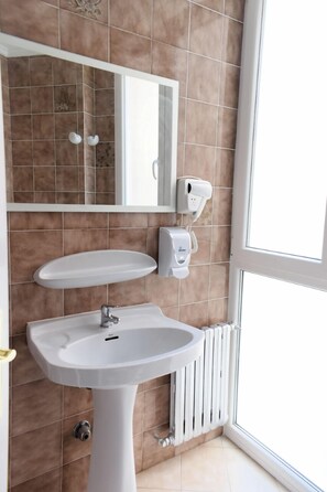 A bathroom with a pedestal sink, a mirror, and a towel dispenser. - Alojamientos Puerto Príncipe (Santander)