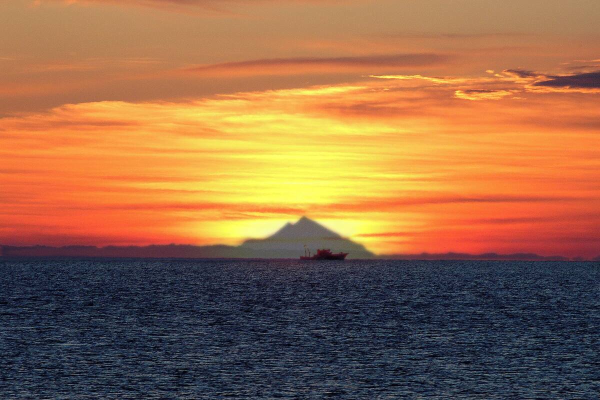 Un atardecer sobre una masa de agua con un barco a lo lejos.