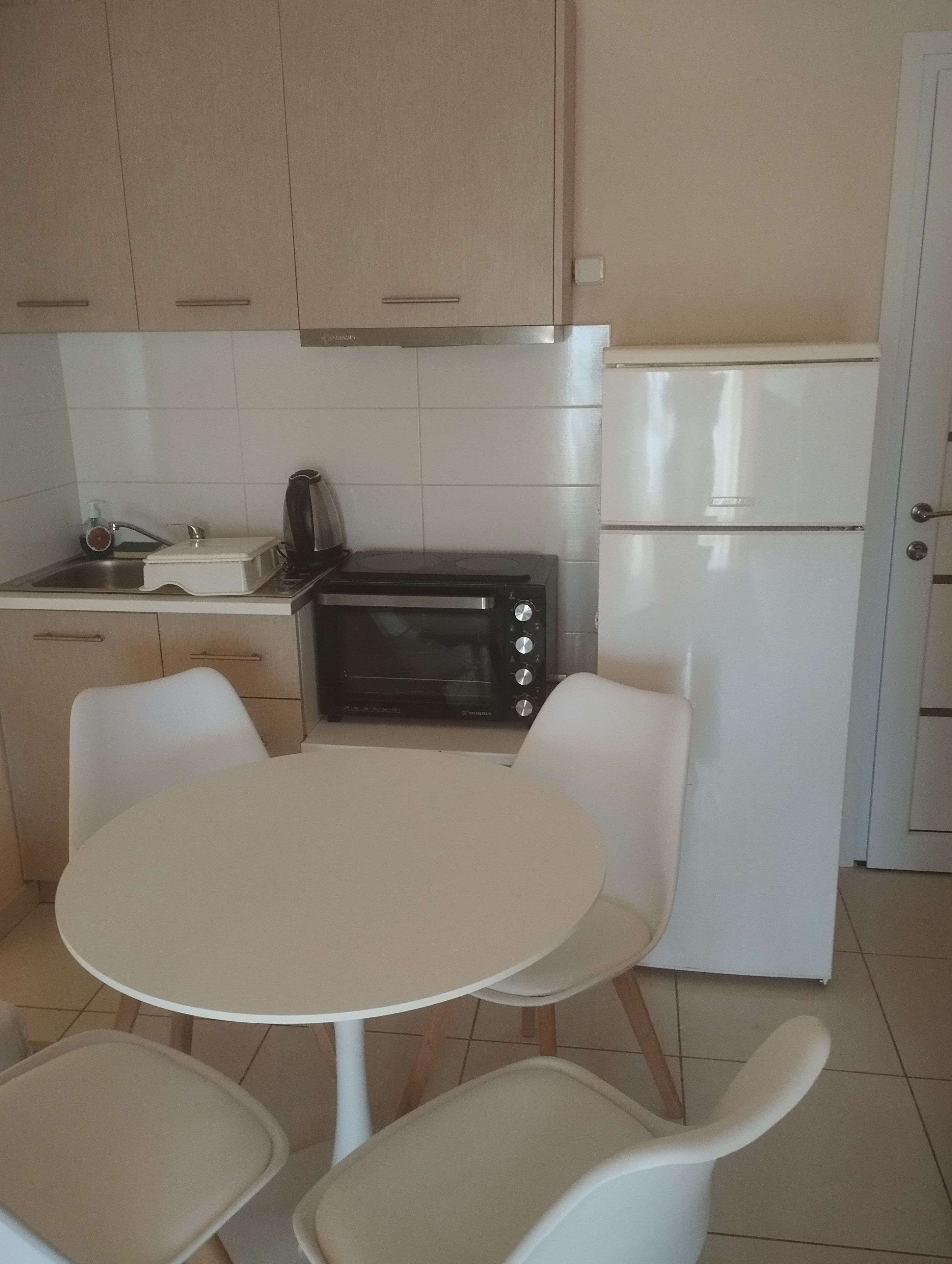 A compact kitchen with a white table and chairs, a black microwave, and a white refrigerator.