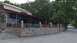 Ein Gebäude mit überdachter Außenbestuhlung, Steinmauern und einer gepflasterten Straße.