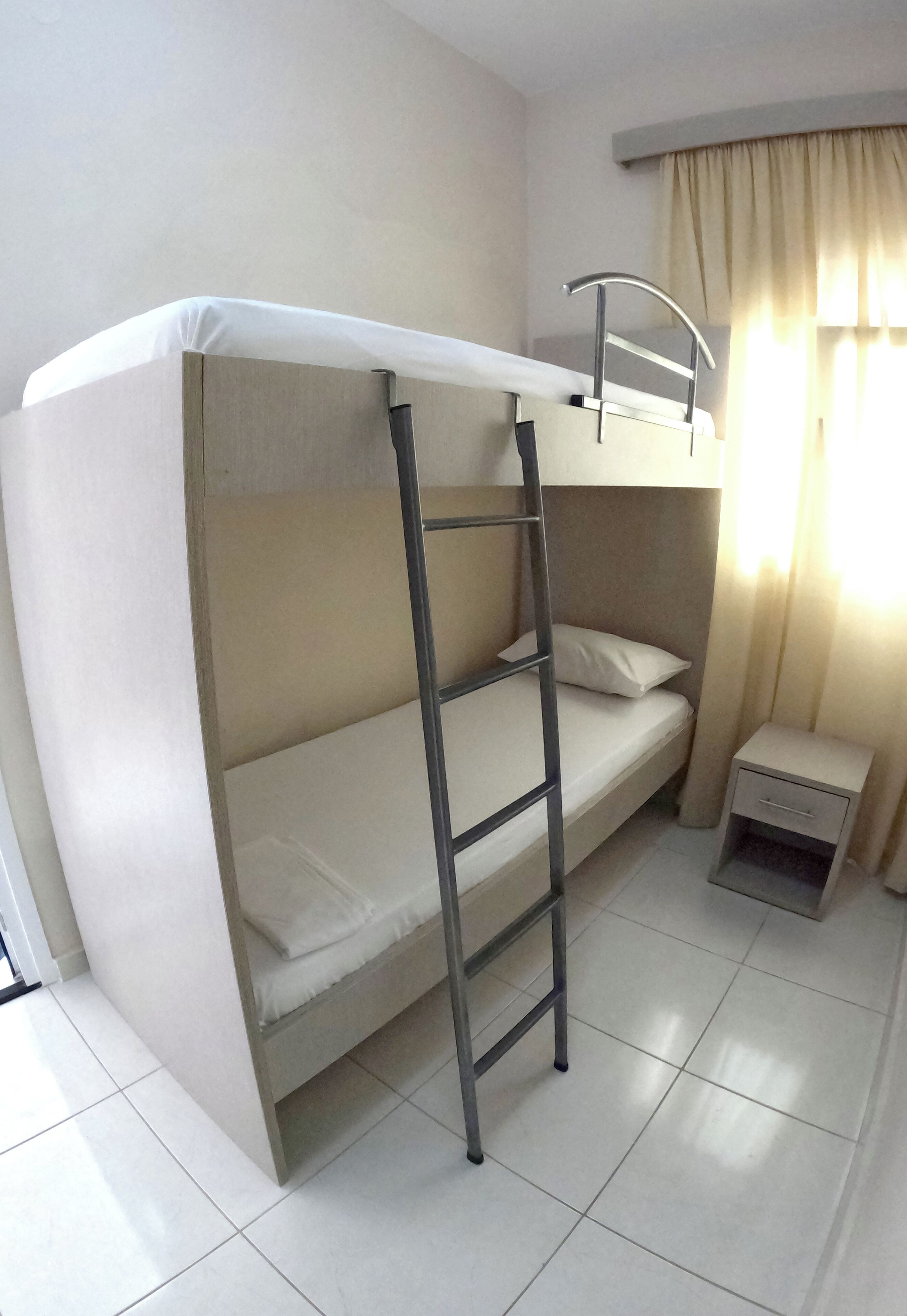 A bunk bed with a ladder, a bedside table, and a window with curtains.