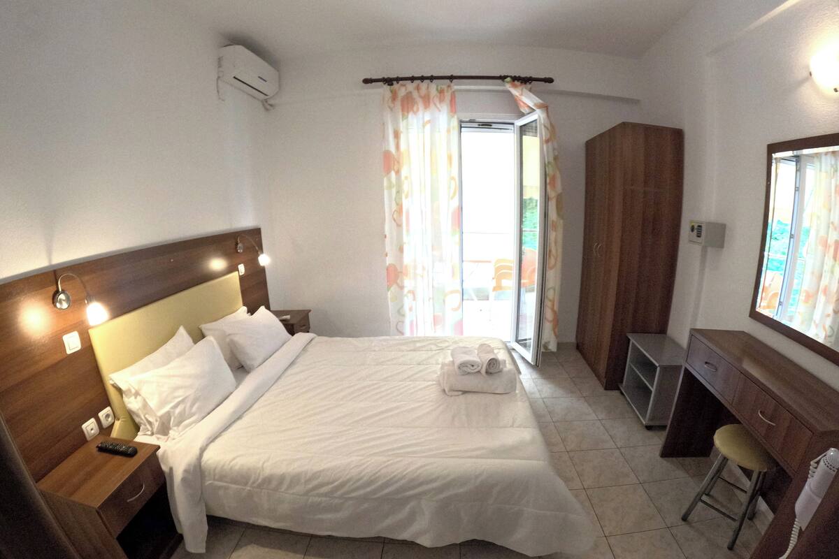 Una habitación de hotel con una cama grande, un escritorio, una silla, un armario y una ventana con cortinas.