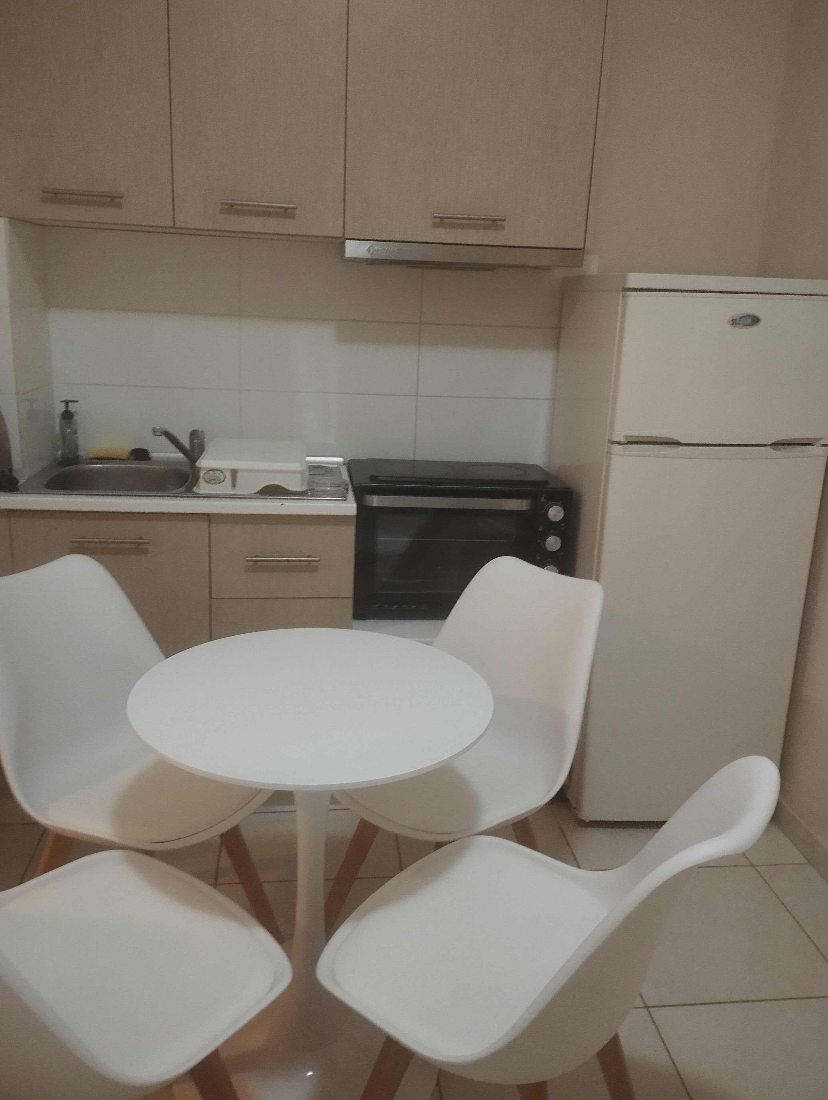 Una cocina con una mesa redonda y cuatro sillas, un fregadero, un tostador y un refrigerador.