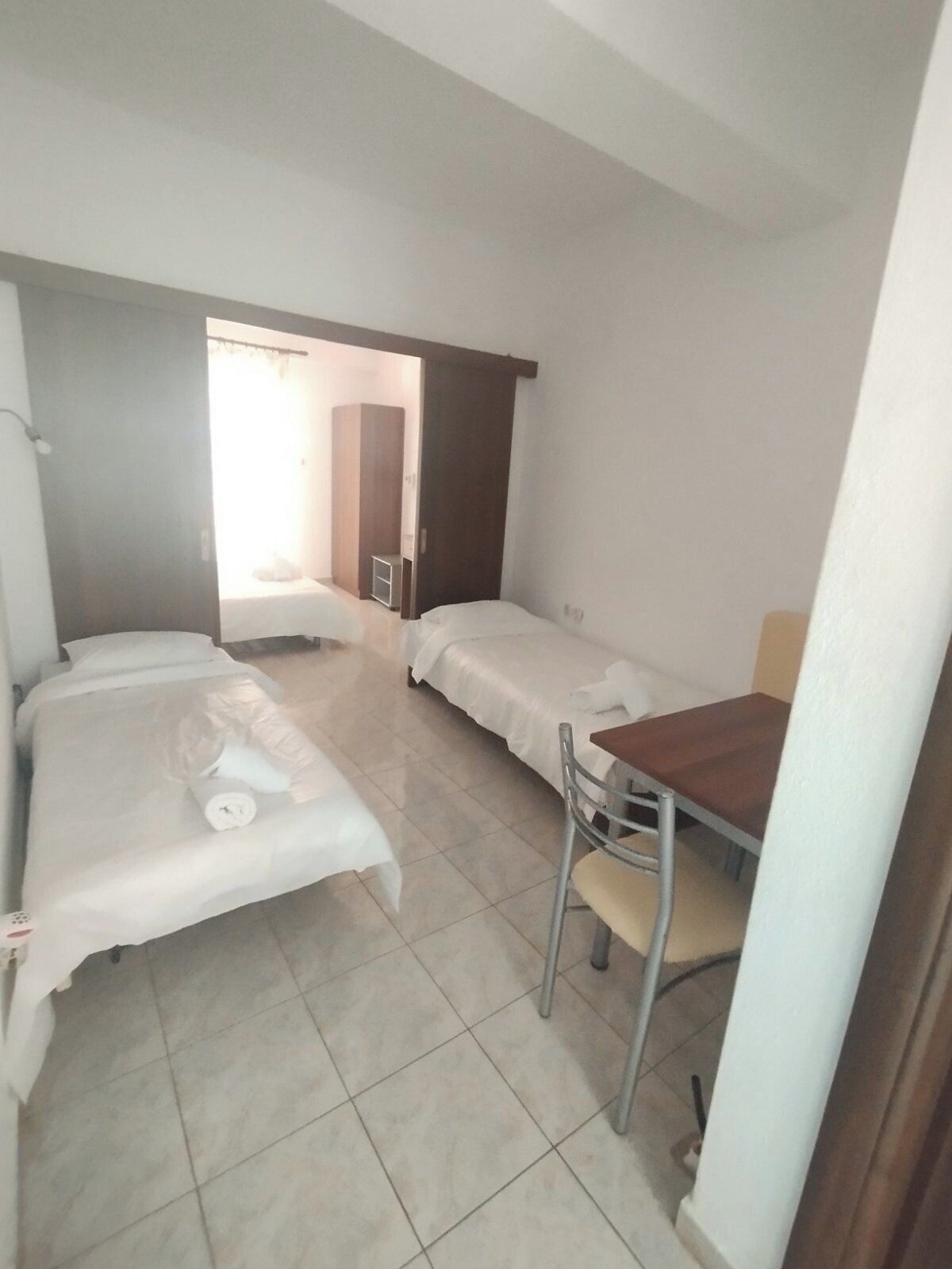 Een kleine, schone kamer met twee eenpersoonsbedden, een tafeltje en een stoel.
