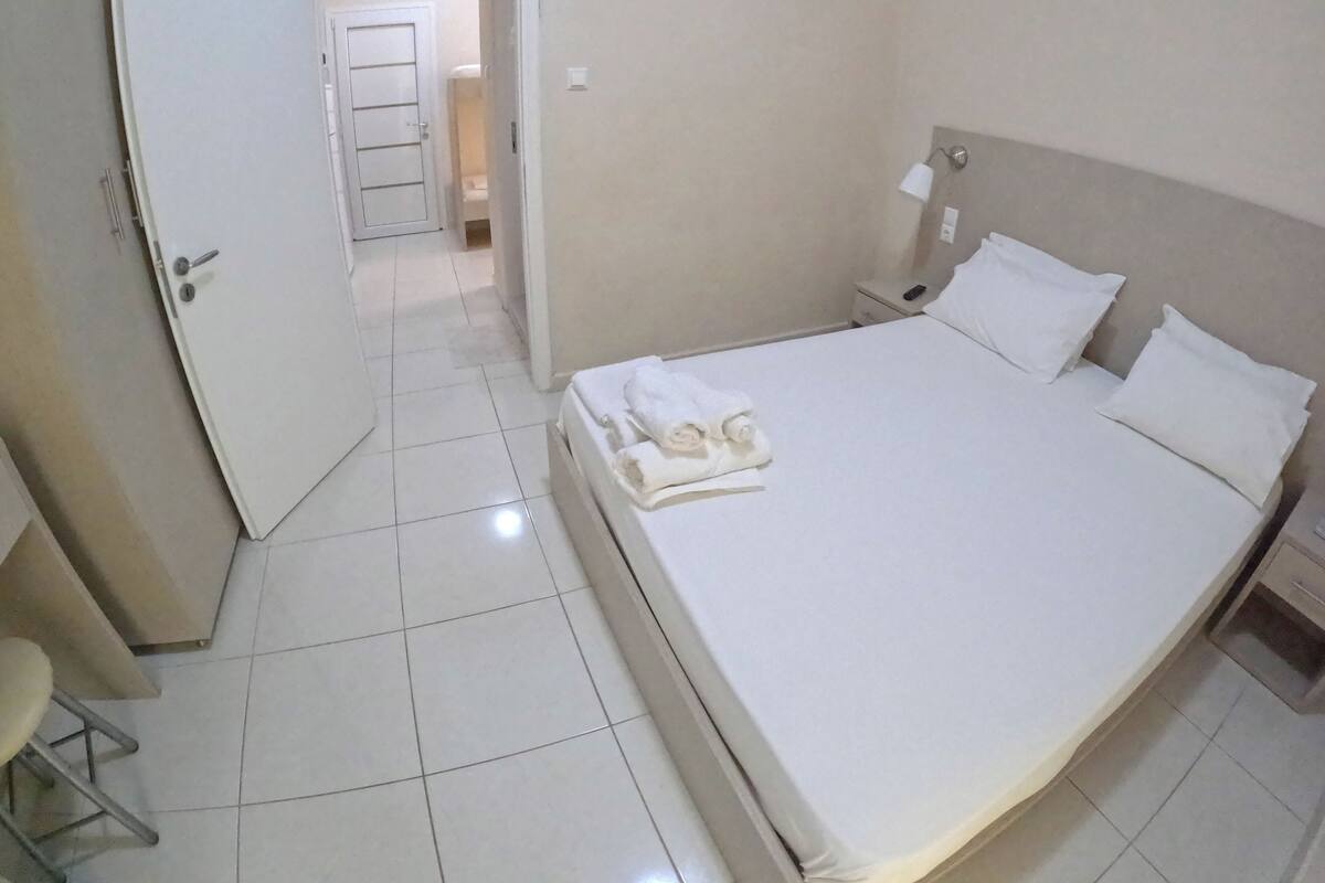 Habitación de hotel con cama, mesita de noche, una silla y un baño visible a través de una puerta abierta.